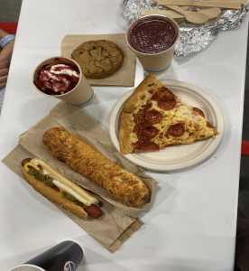 The picture was taken of Redwood City’s Costco food. Featured in the photo there is a chicken bake, hot dog, pizza slice, strawberry sunday, fruit smoothie, and a chocolate chip cookie.